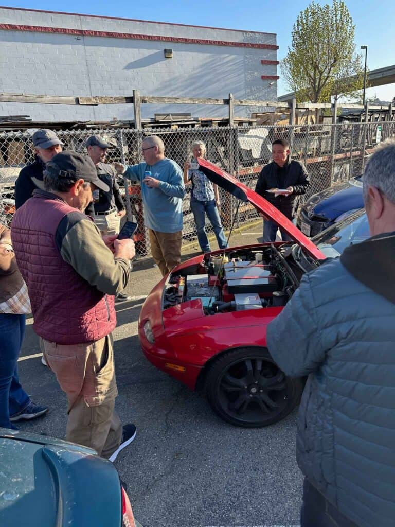 Image showcasing Earthling Automotive customers looking at a Mazda Miata with a Tesla motor and battery EV conversion and swap
